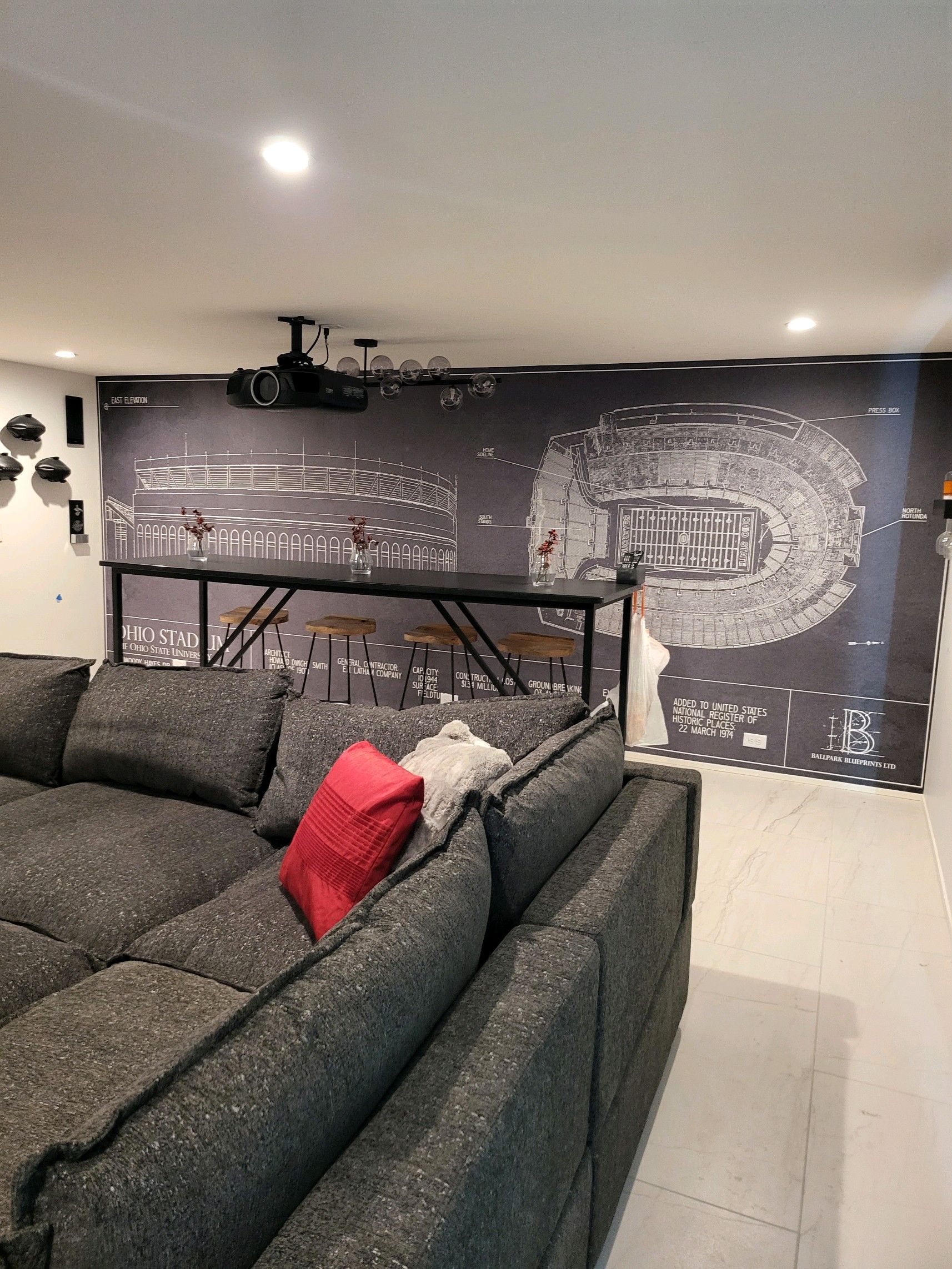 Cozy home theater with gray sectional sofa, bar, cityscape wallpaper, and a projector.