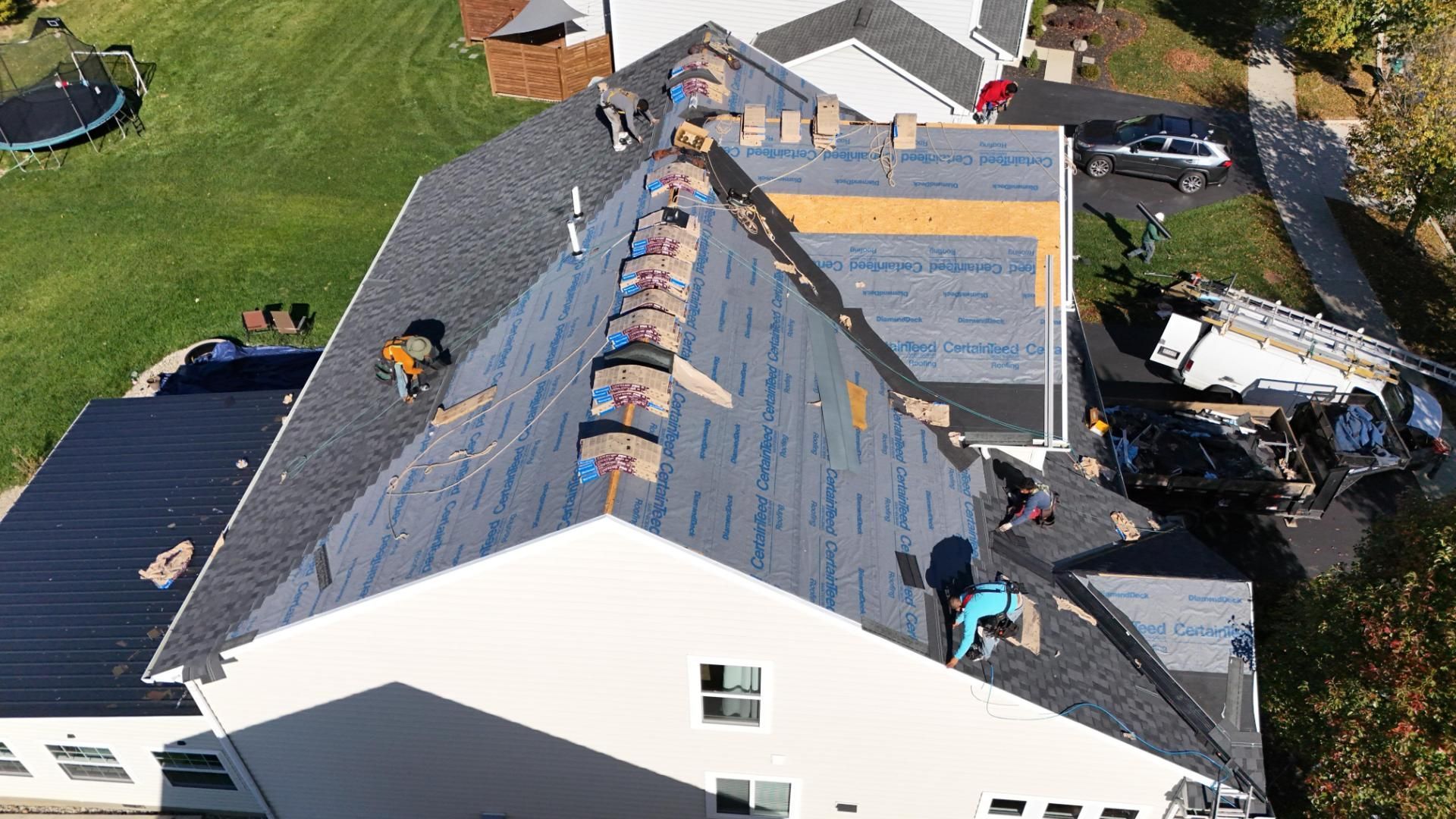 Roofers working on a residential roof. Some shingles removed, blue underlayment visible.