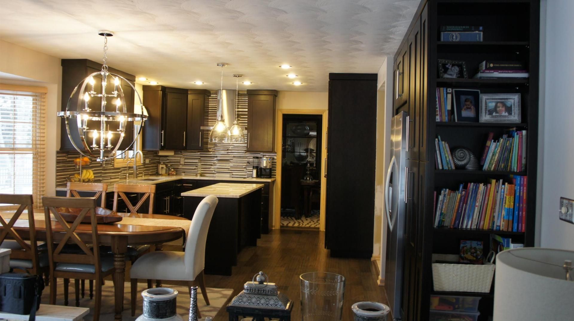 A modern kitchen and dining area with dark cabinets, an island, and a bookshelf.