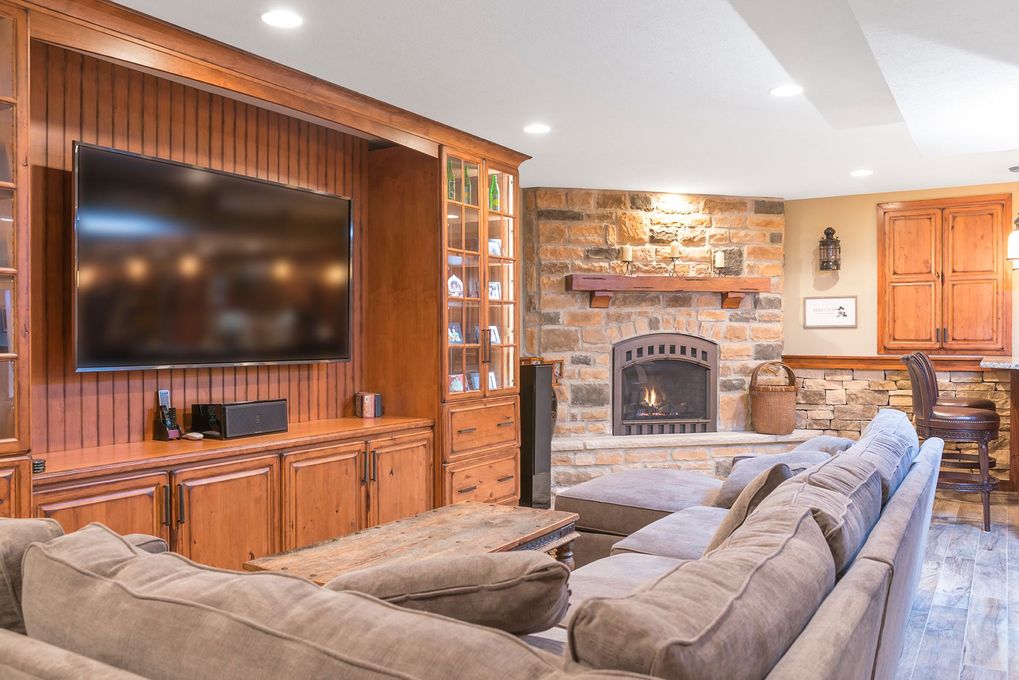 Cozy living room with large TV, stone fireplace, wood built-ins, and sectional sofa.