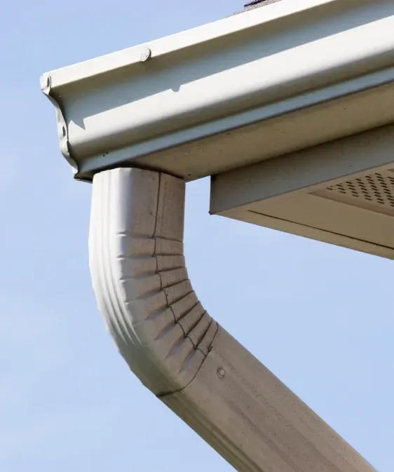 Gray rain gutter and downspout attached to a white roof edge, angled against a blue sky.