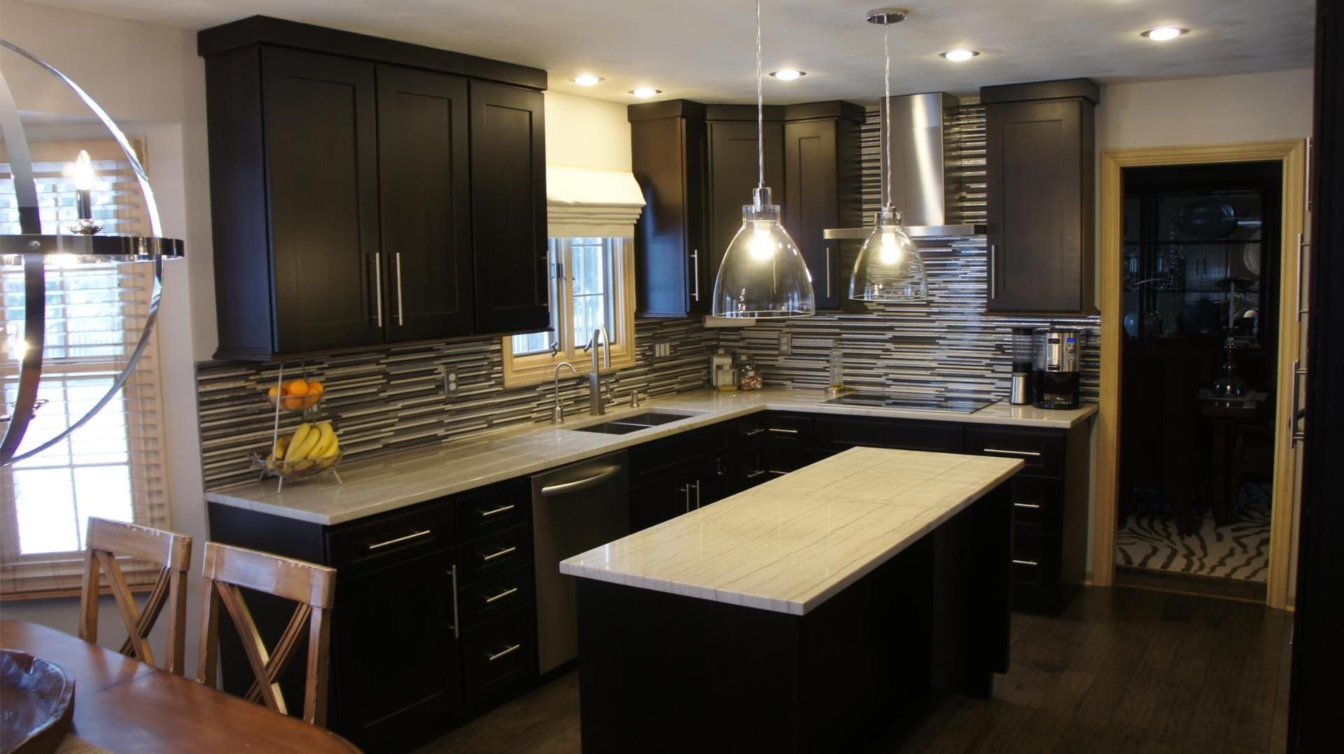 Dark kitchen with black cabinets, white countertops, and a gray tiled backsplash.