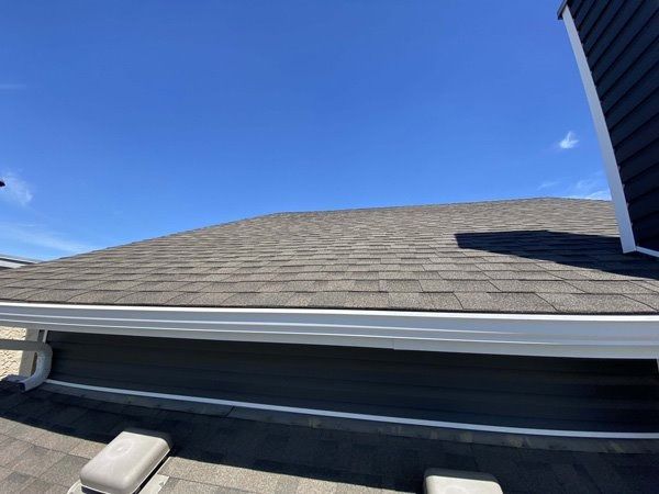 A dark gray shingle roof with white gutters against a clear blue sky.
