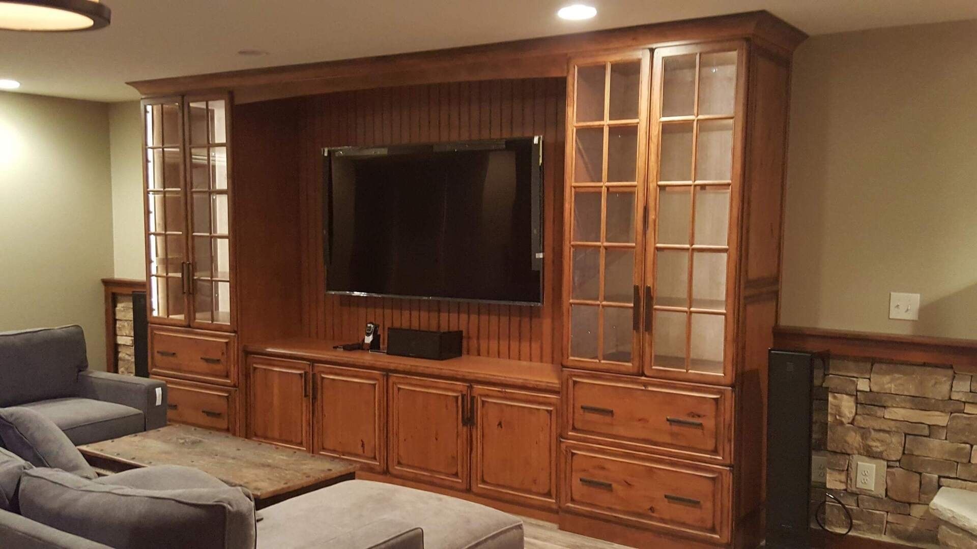 Wooden entertainment center with TV, cabinets, and glass-doored shelves; in a living room setting.