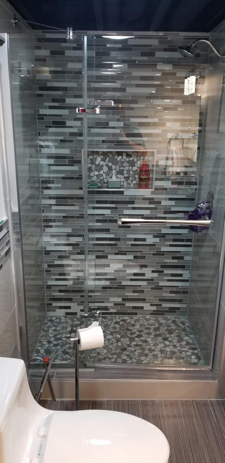Shower stall with glass doors, tiled walls and floor, and a toilet next to it.