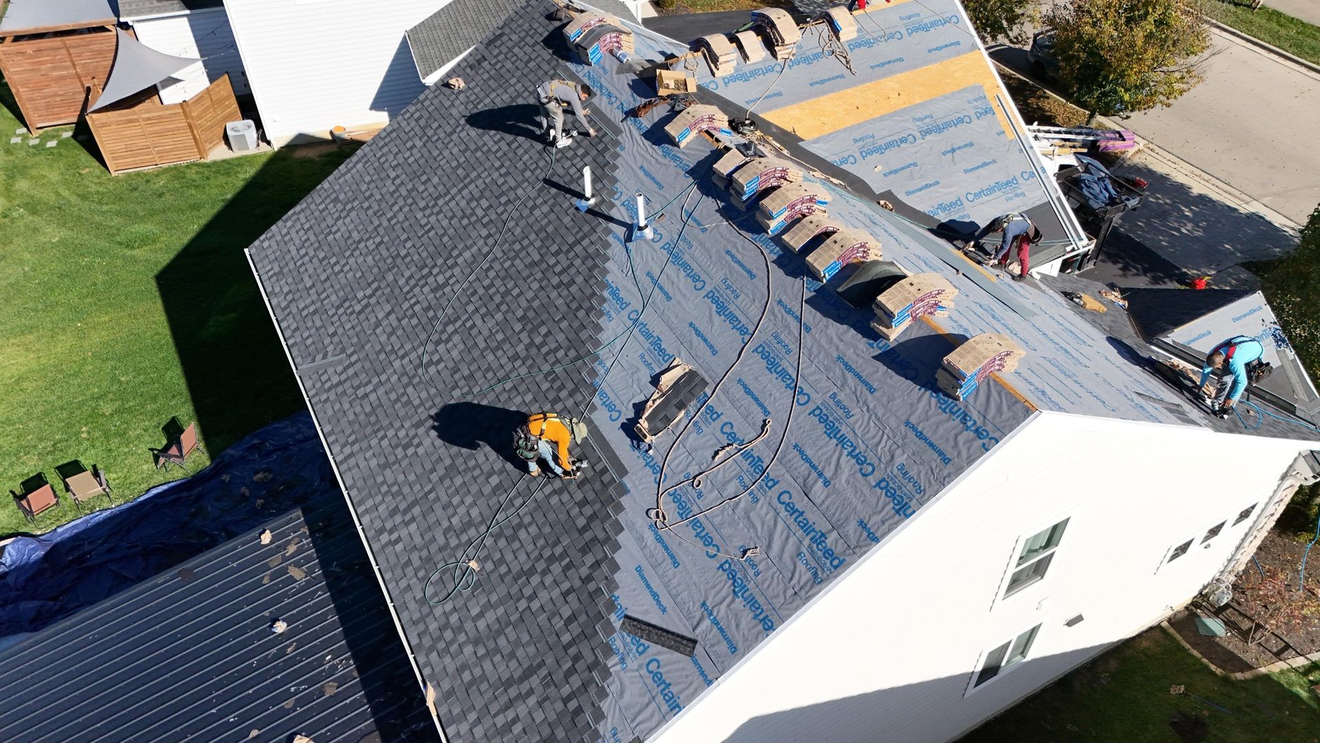 Roofers installing asphalt shingles on a residential roof; tools and materials visible.