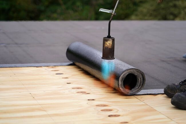Roofers installing asphalt shingles on a residential roof; tools and materials visible.