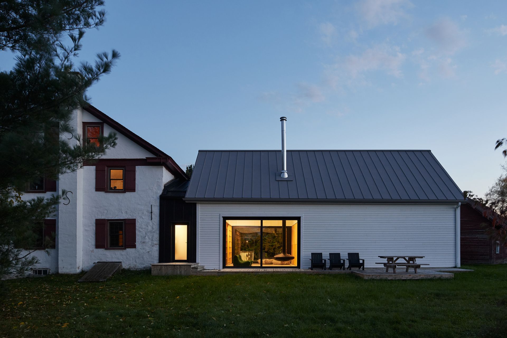 Une maison blanche avec un toit noir et une table de pique-nique devant.