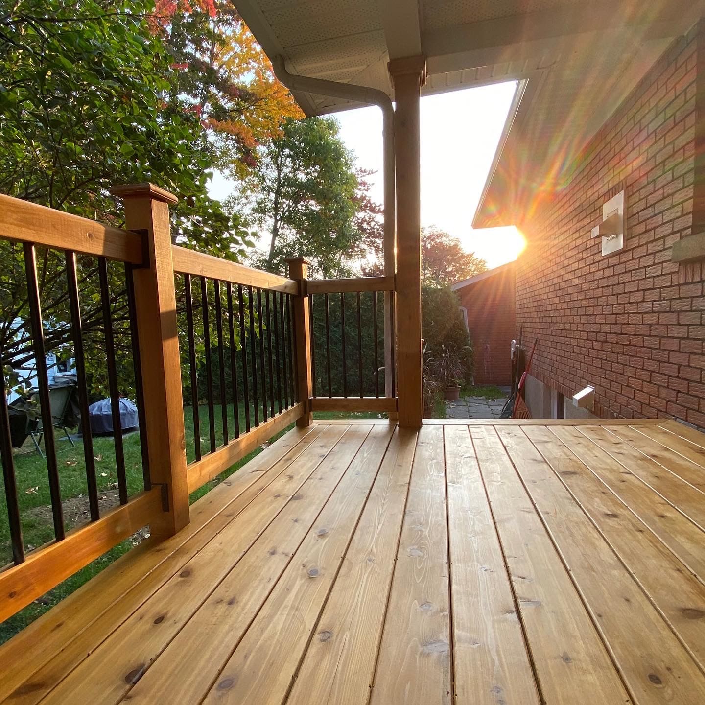 Une terrasse en bois avec une balustrade en métal et une maison en briques en arrière-plan.