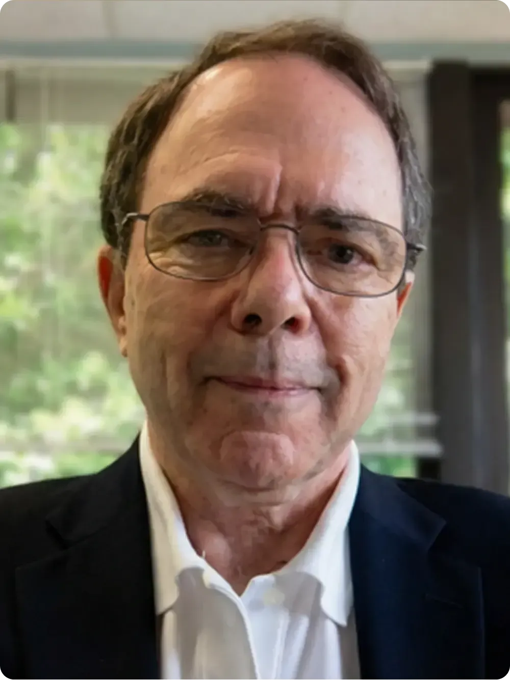 Man wearing glasses, white shirt, and dark jacket, looking at the viewer.