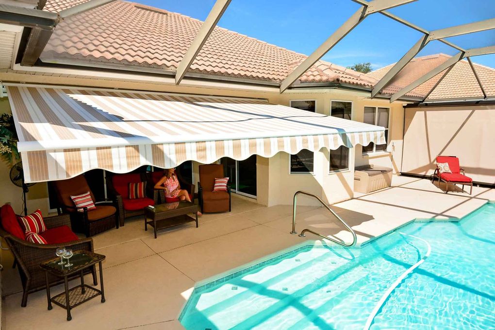 a woman sits on a patio next to a swimming pool under an awning .