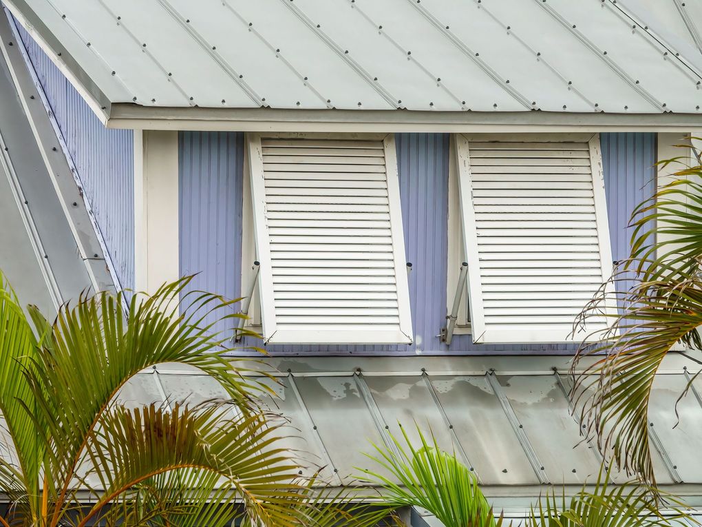 a house with white shutters on the windows and palm trees in front of it .