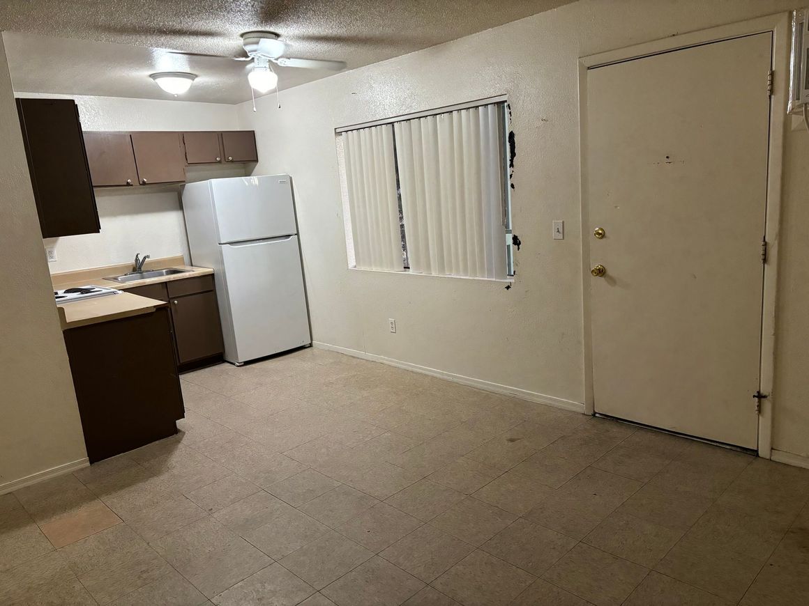 A kitchen with a refrigerator , sink , cabinets and a door.