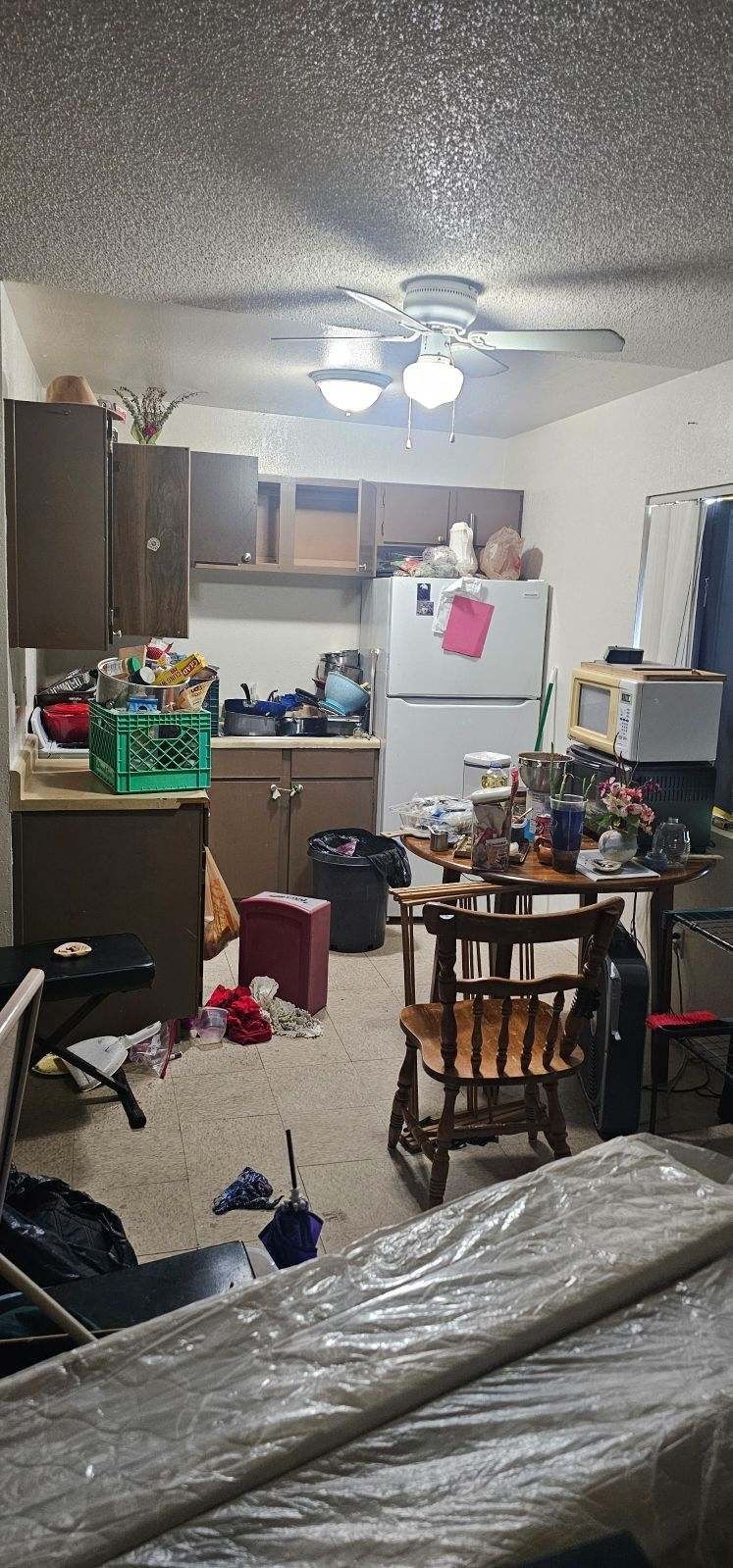 A kitchen with a refrigerator , a table , chairs , and a ceiling fan.