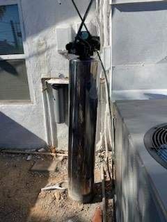 A water filter is sitting next to an air conditioner on the side of a building.