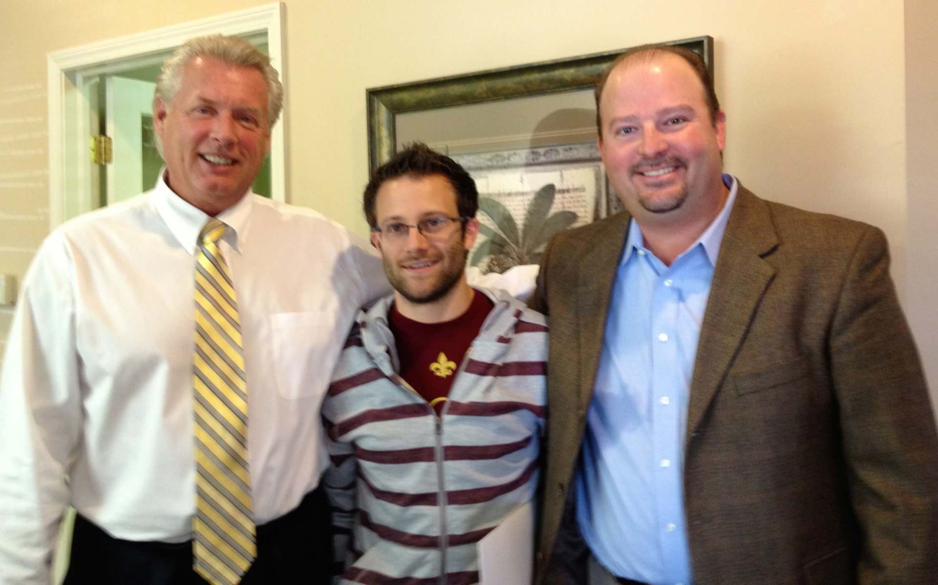 Three men posing for a picture with one wearing a striped shirt
