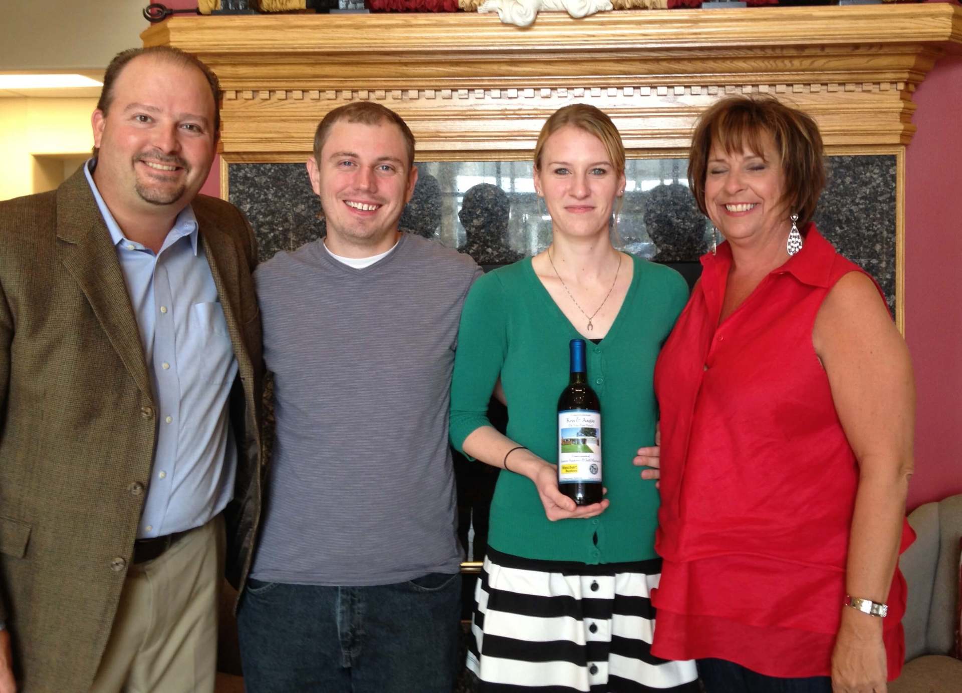 A woman holding a bottle of wine stands between two men and a woman