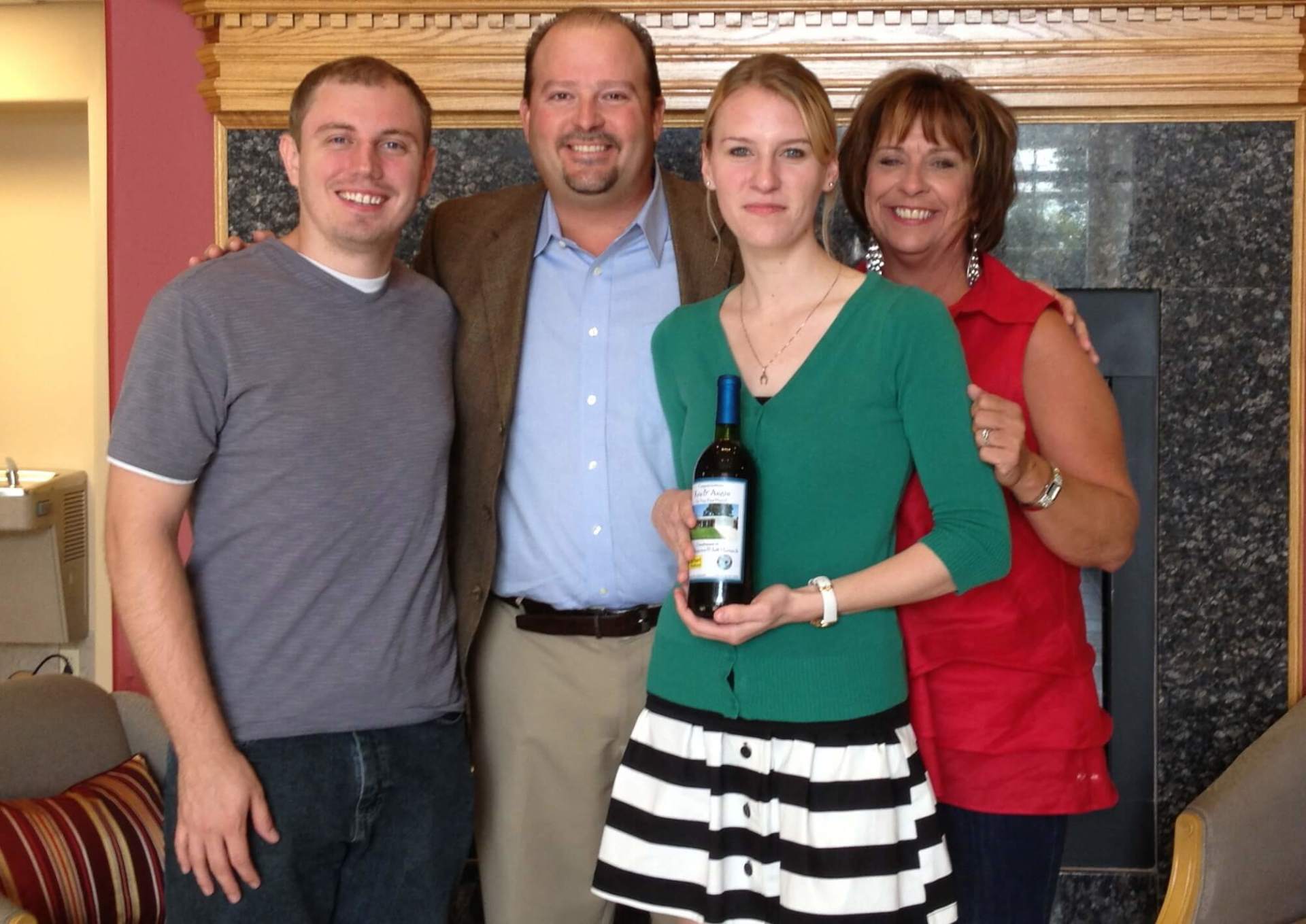 A woman is holding a bottle of wine while posing for a picture with her family