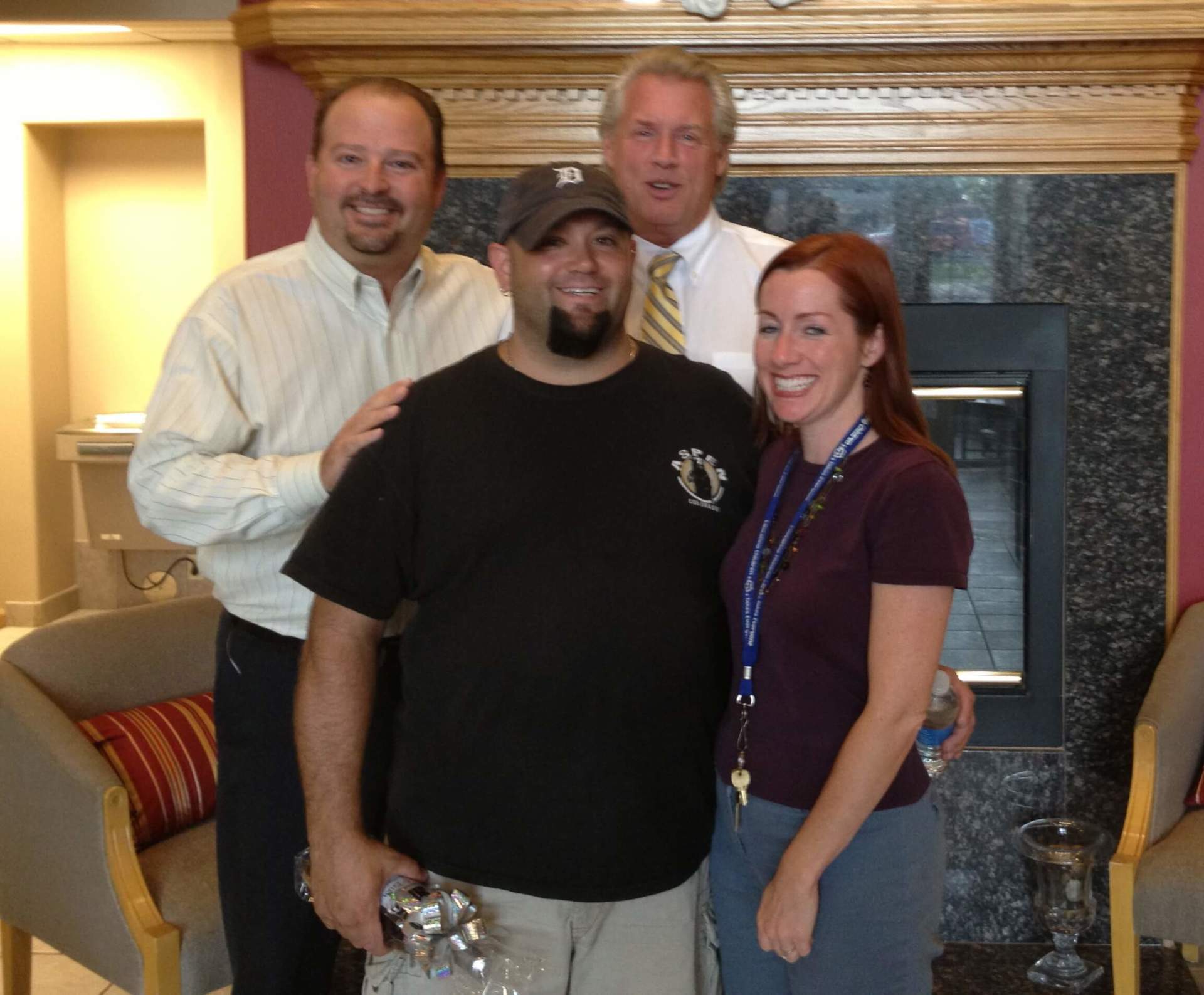 Three men and a woman pose for a picture in front of a fireplace