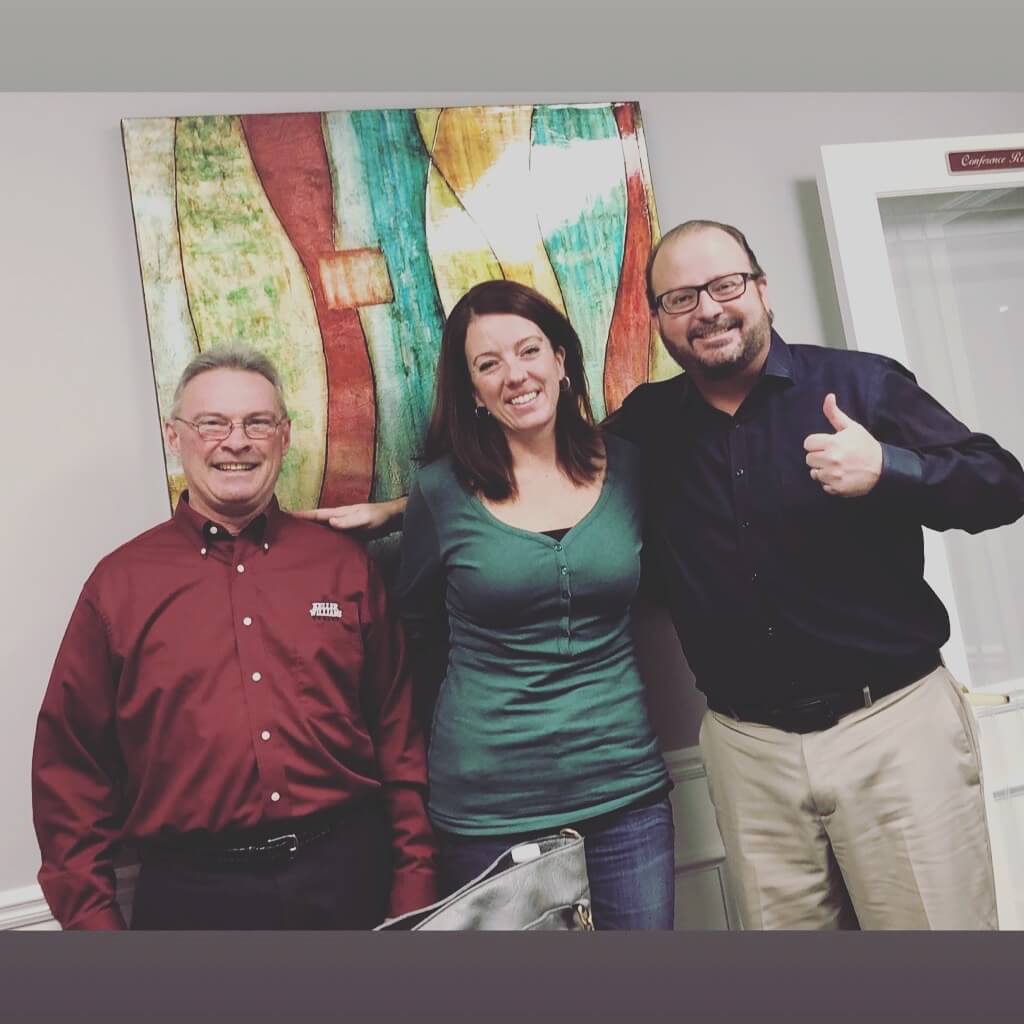 Three people posing for a picture in front of a painting