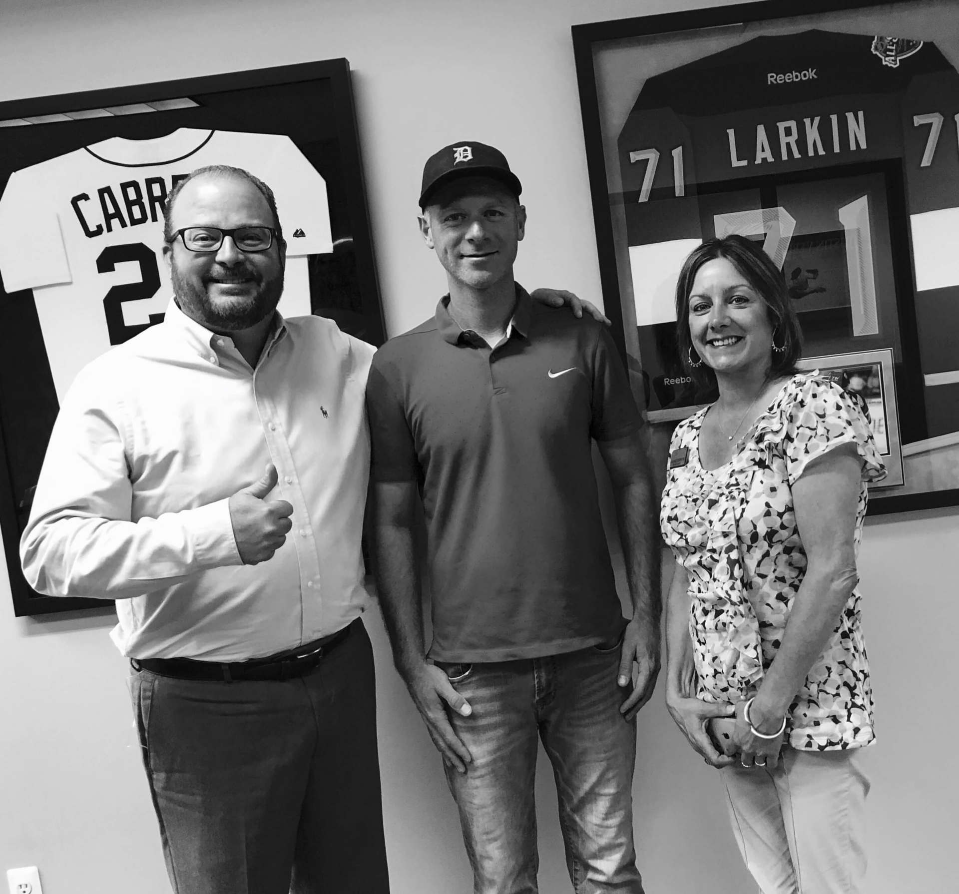 Three people are posing for a picture in front of a framed baseball jersey.