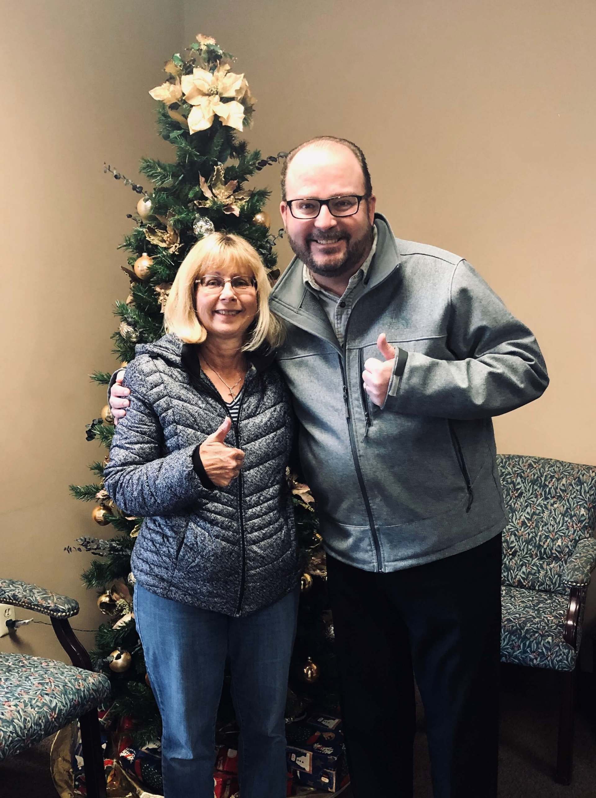 A man and a woman are posing for a picture in front of a christmas tree.