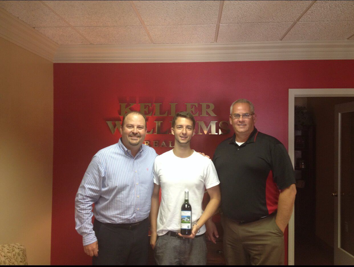 Three men are posing for a picture in front of a wall that says keller williams