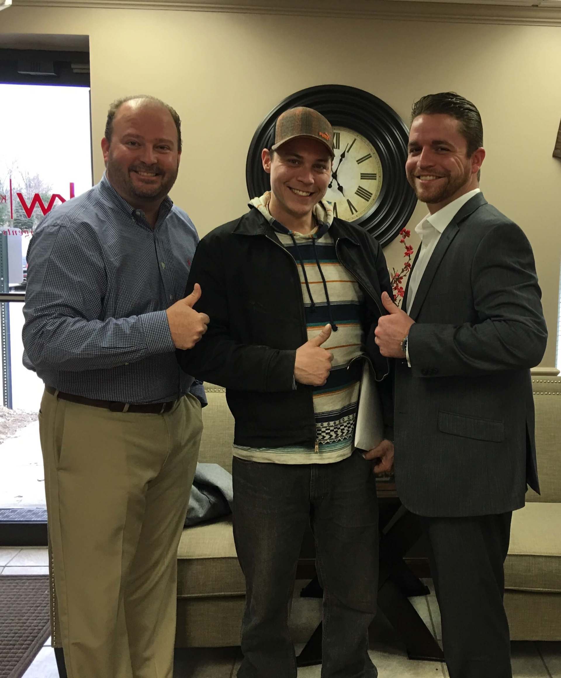 Three men are posing for a picture in front of a clock