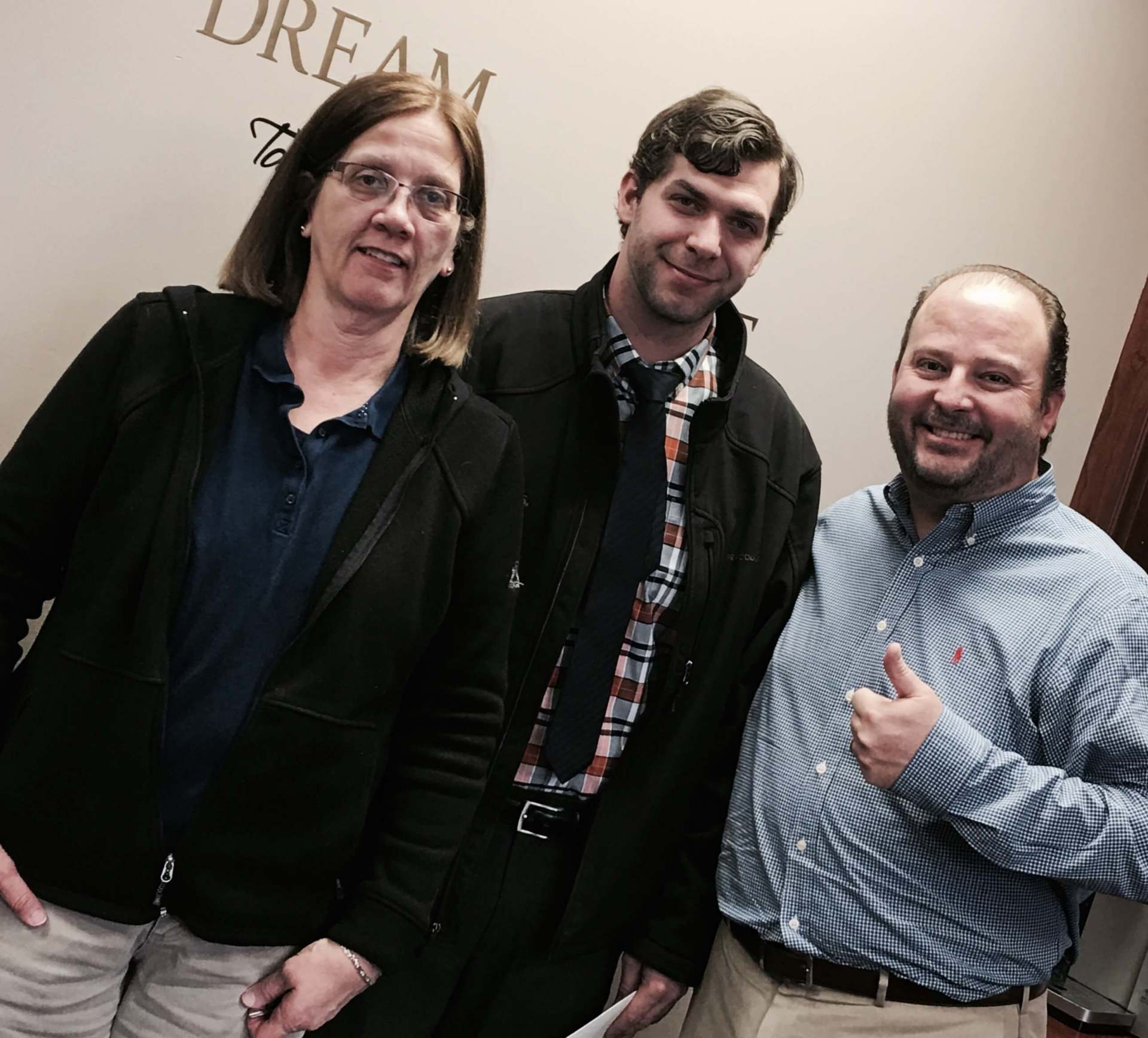 Three people standing in front of a wall that says dream
