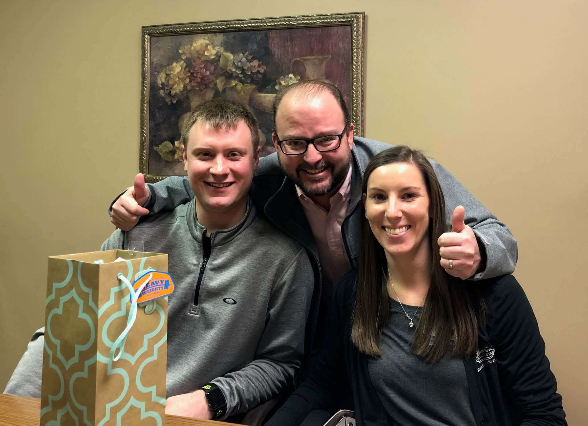 A man and two women are posing for a picture with a gift bag.