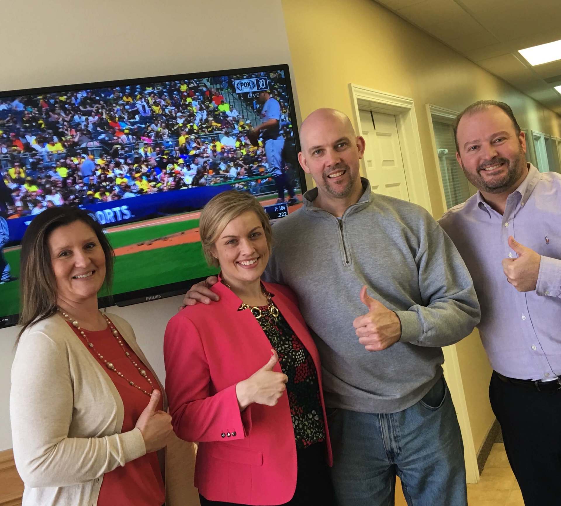 A group of people giving a thumbs up in front of a tv.