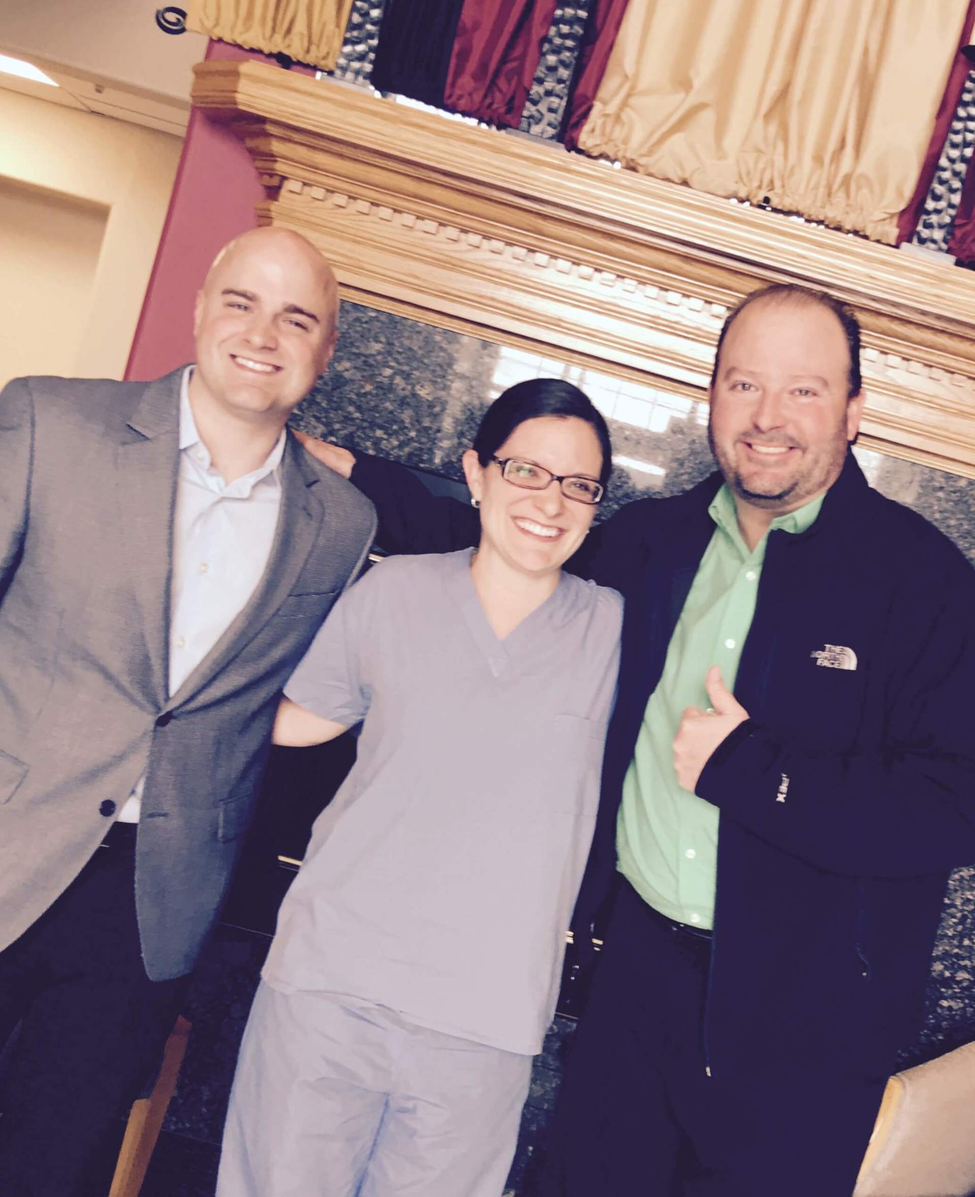 Three people posing for a picture in front of a fireplace.