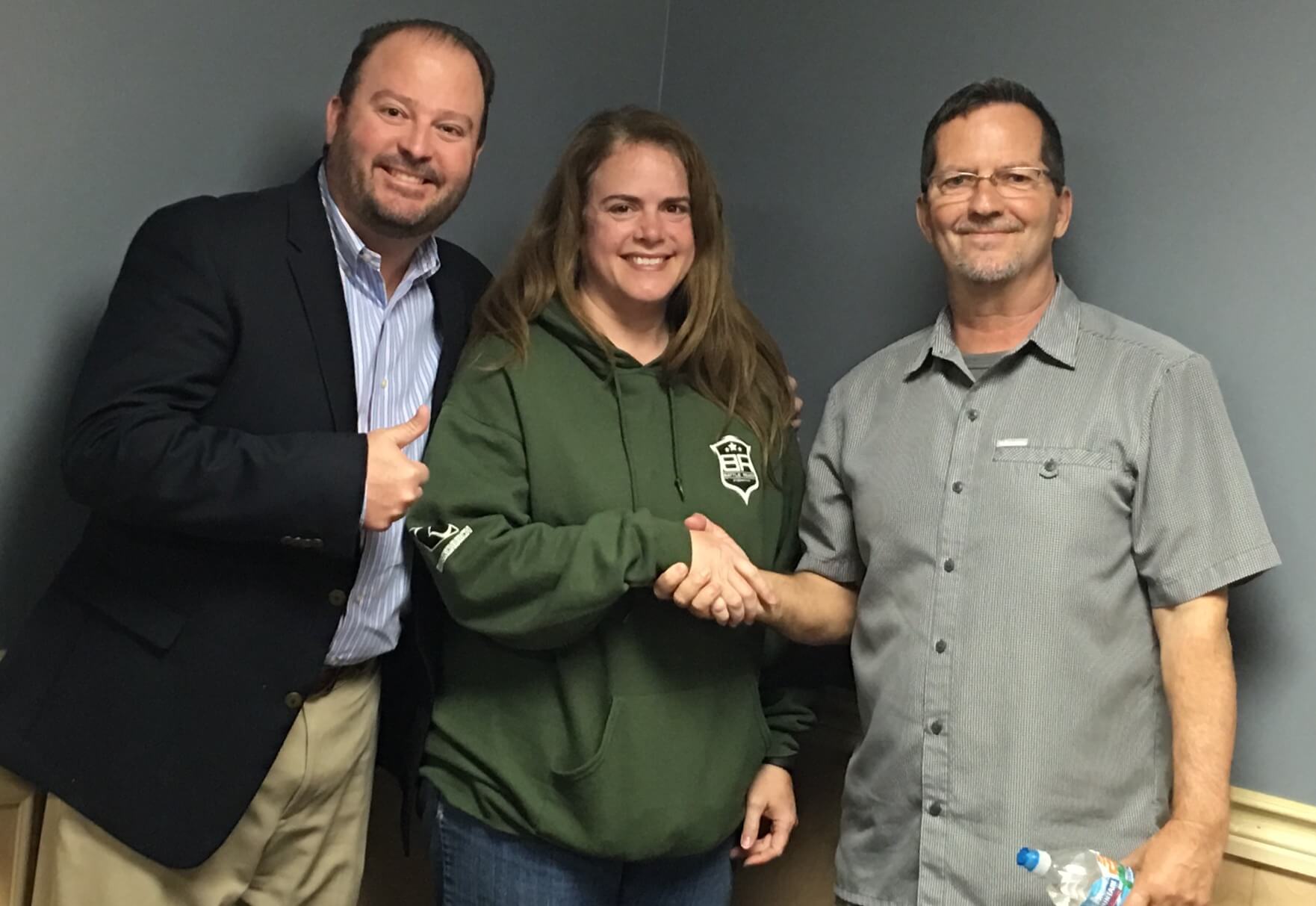 A woman in a green hoodie is shaking hands with two men.