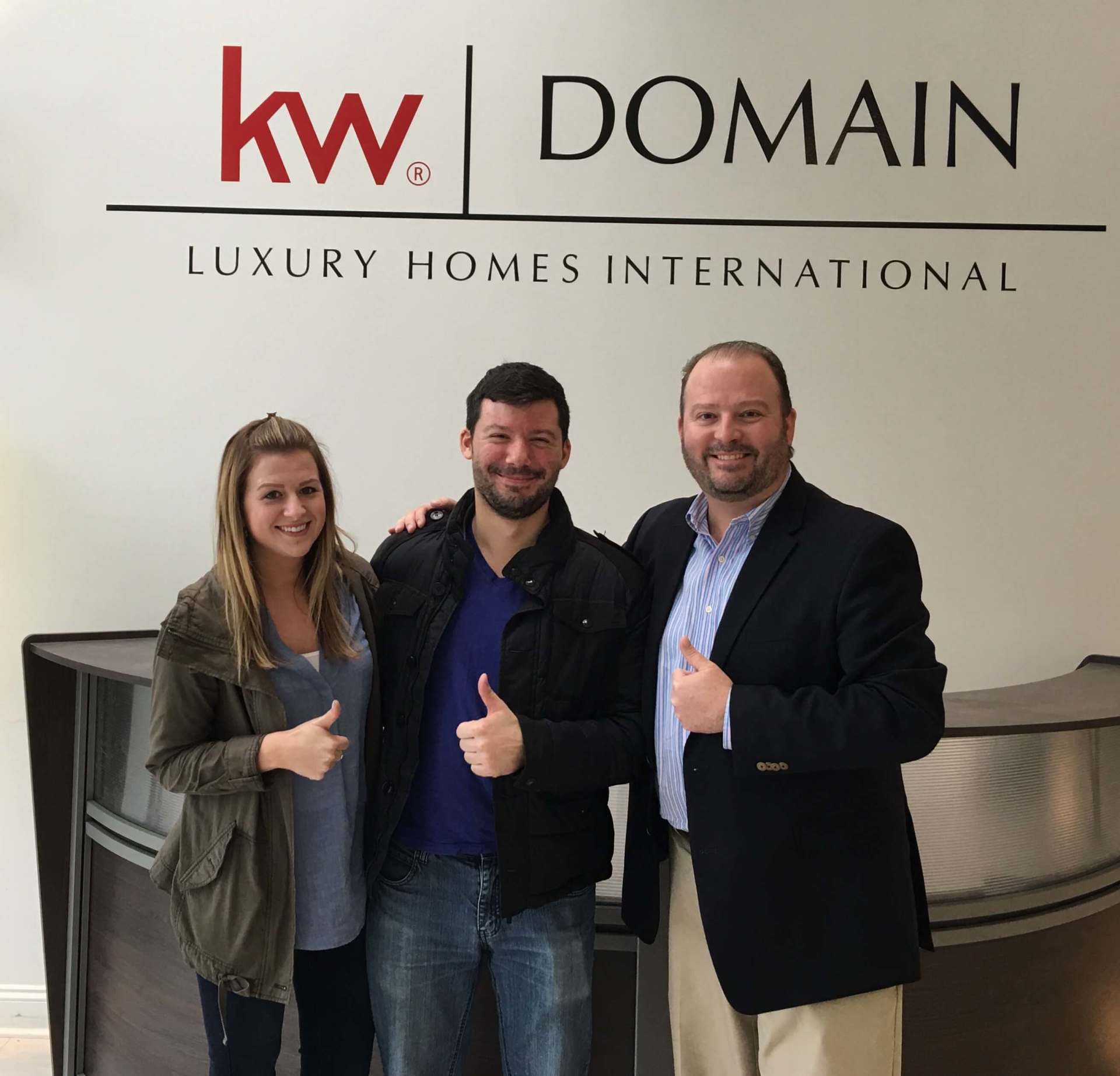 Three people are posing in front of a kw domain sign.
