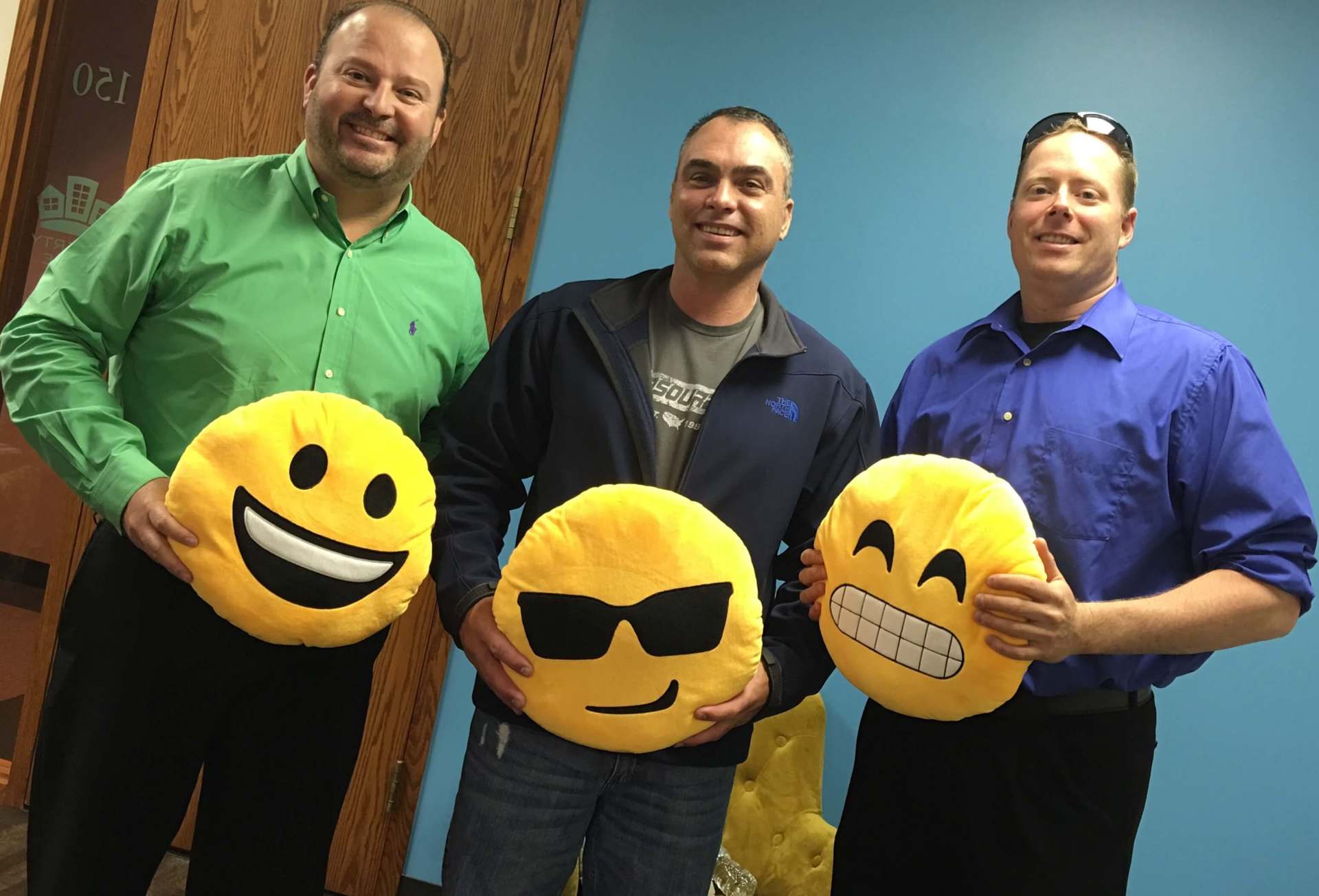 Three men are holding smiley face pillows in their hands.