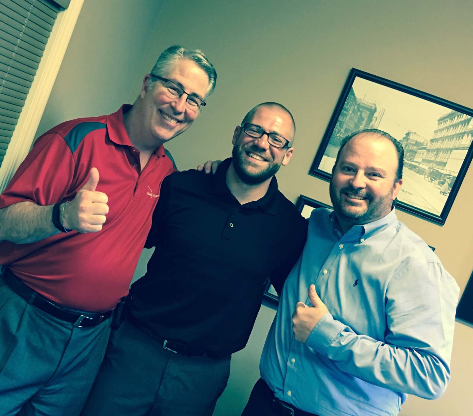 Three men are posing for a picture and one is giving a thumbs up.