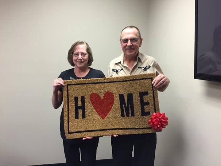 A man and woman are holding a door mat that says home.