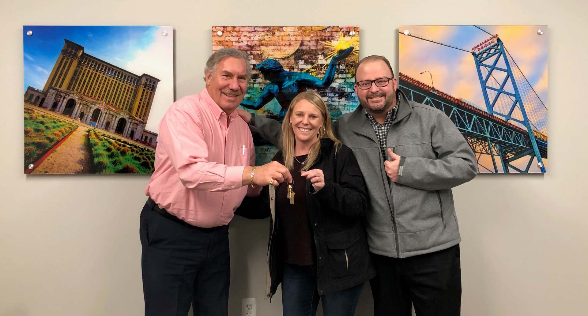 Three people are standing next to each other in front of a wall with pictures on it.