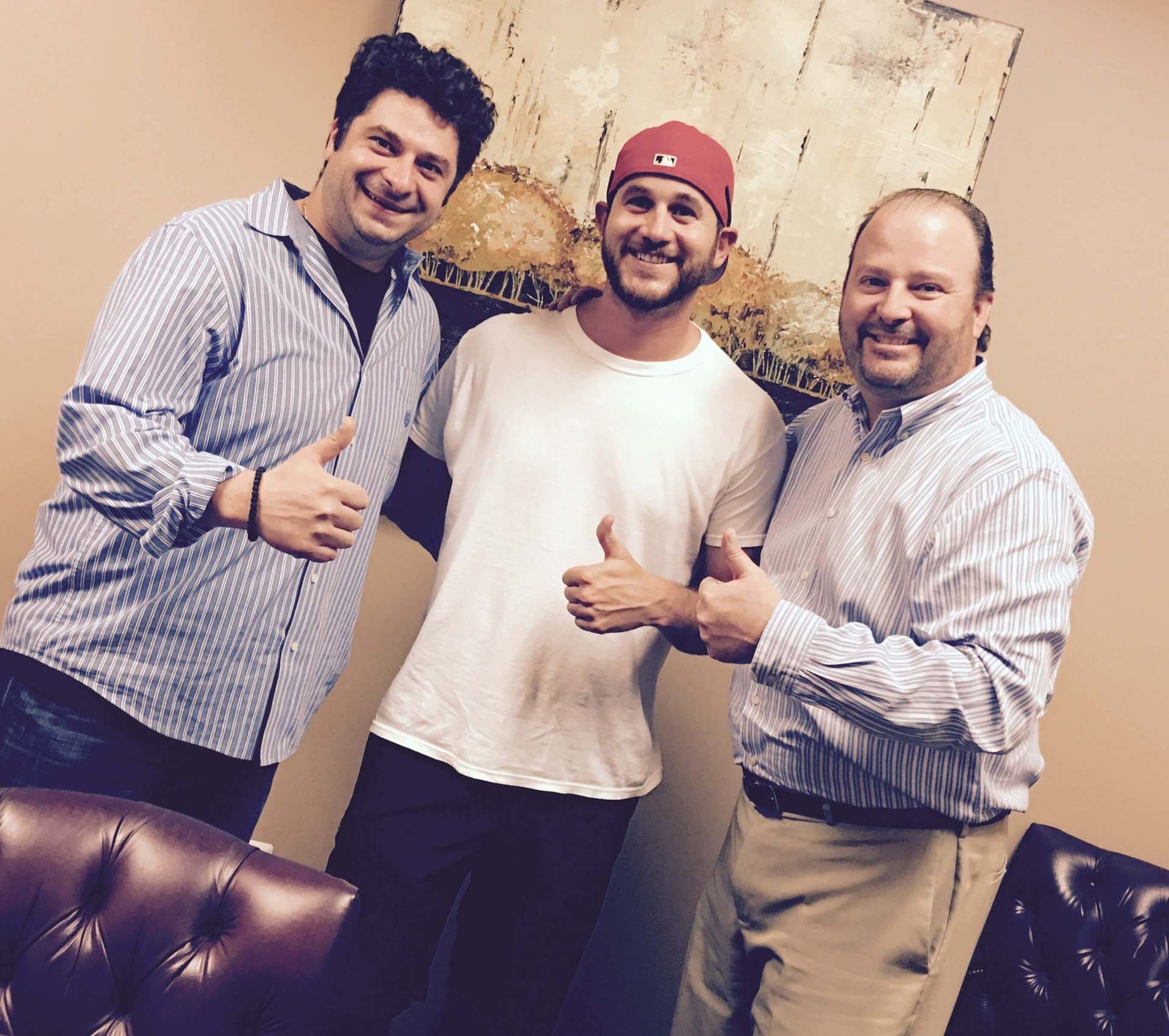 Three men are posing for a picture and one of them is wearing a red hat.