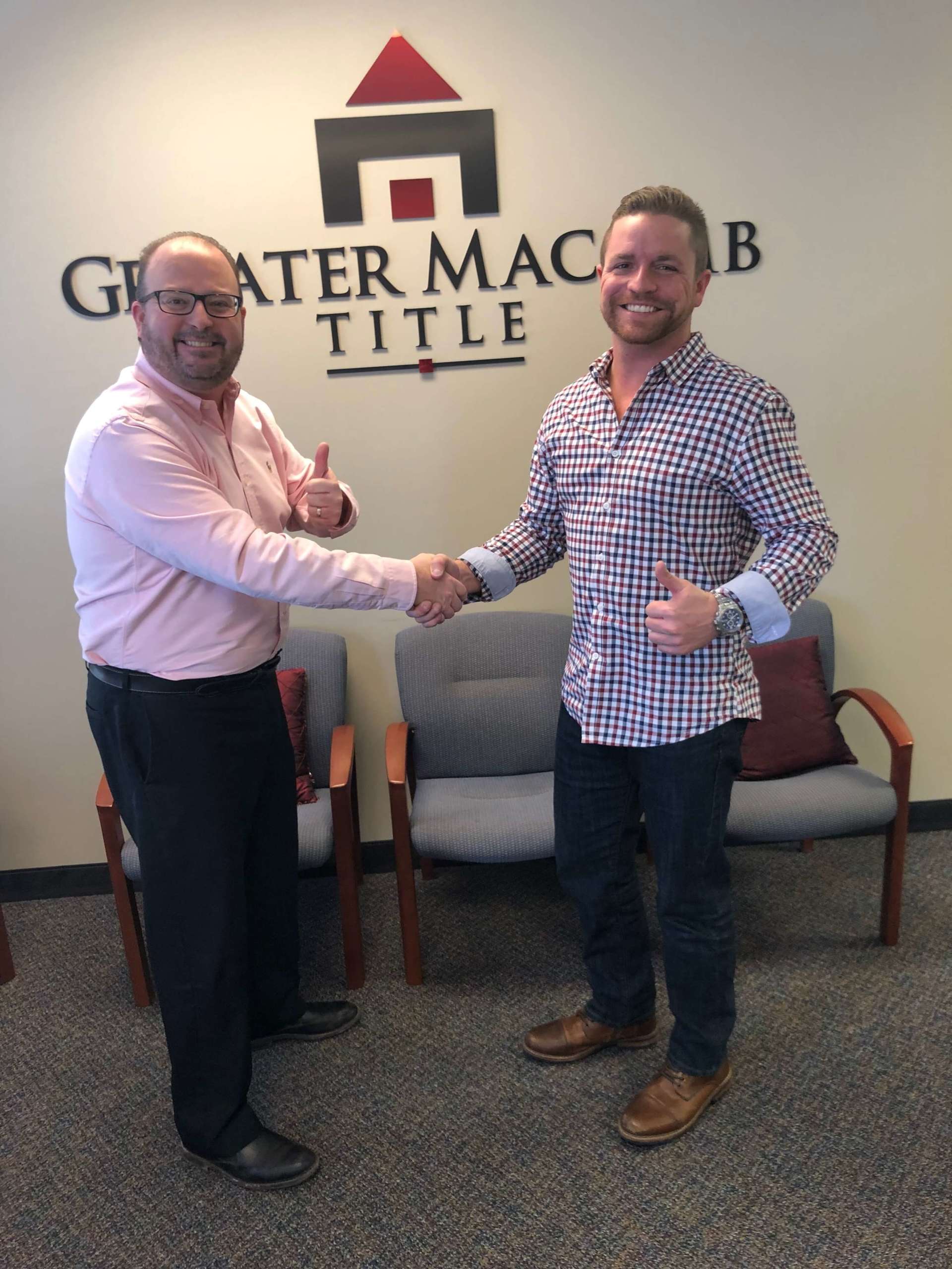 Two men shaking hands in front of a wall that says greater maccab title.
