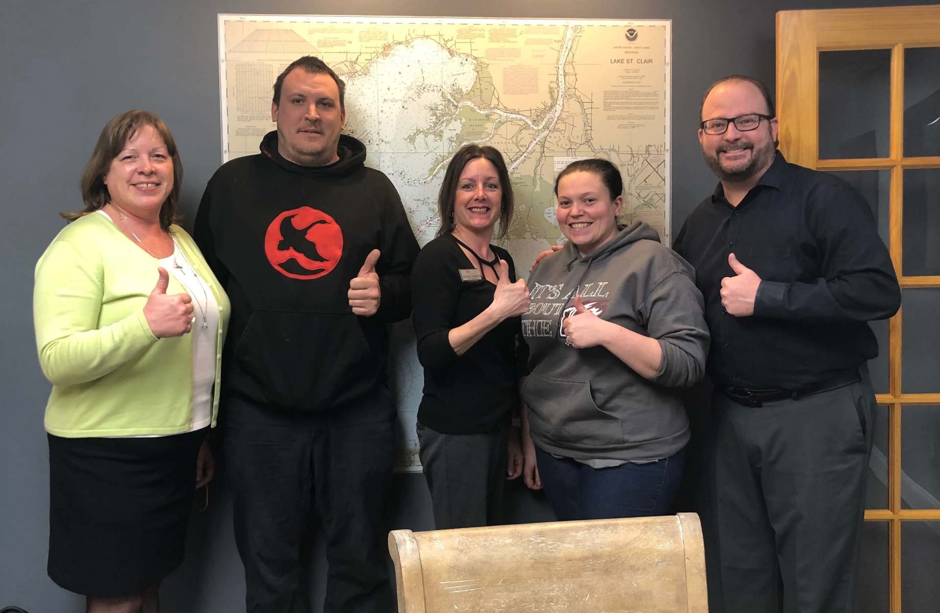 A group of people are giving a thumbs up in front of a map.