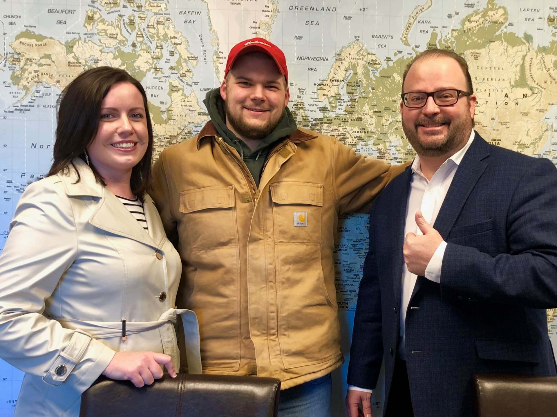 Three people are posing for a picture in front of a map of the world.