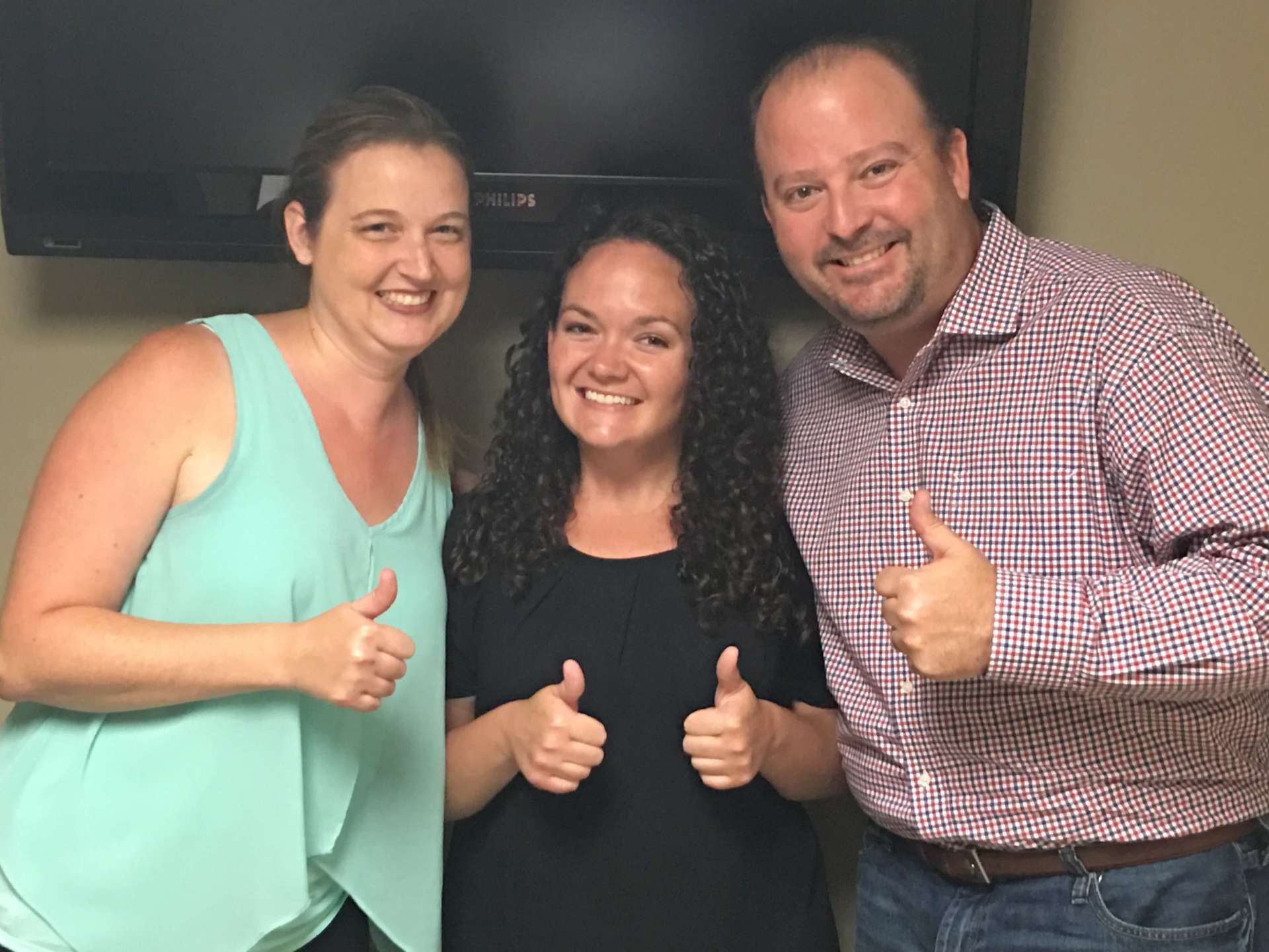 Three people are posing for a picture and giving a thumbs up.