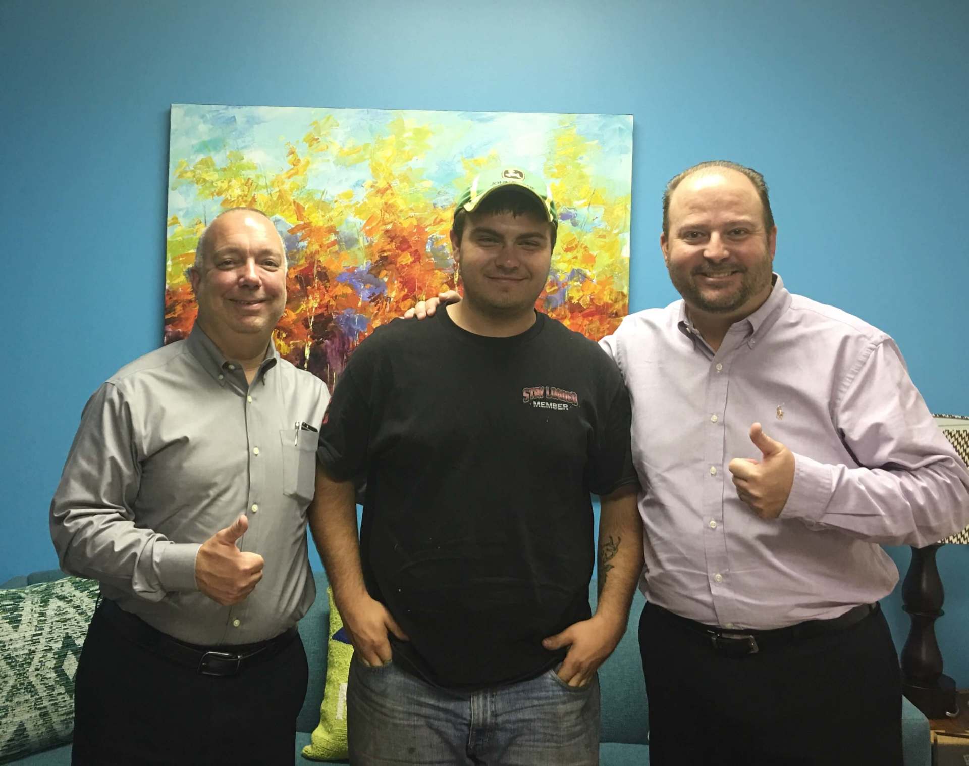 Three men are posing for a picture in front of a painting.
