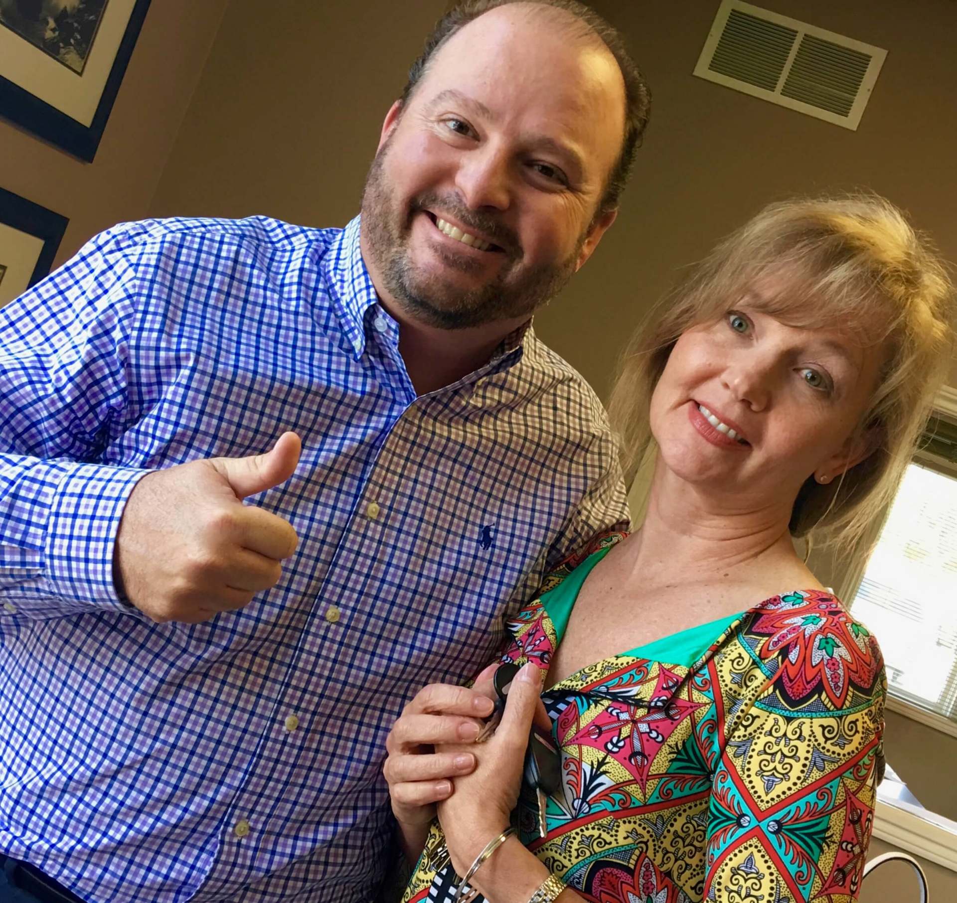 A man and woman are posing for a picture and the man is giving a thumbs up.
