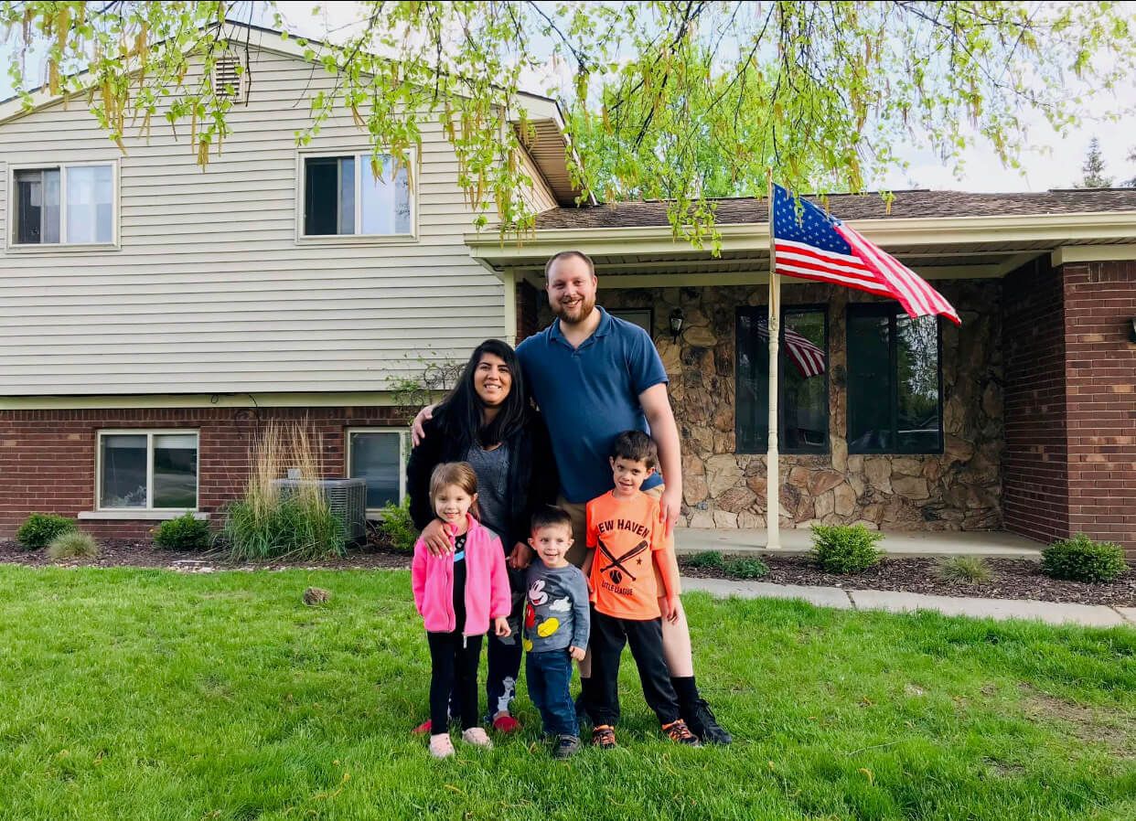 A family is standing in front of a house with an american flag.