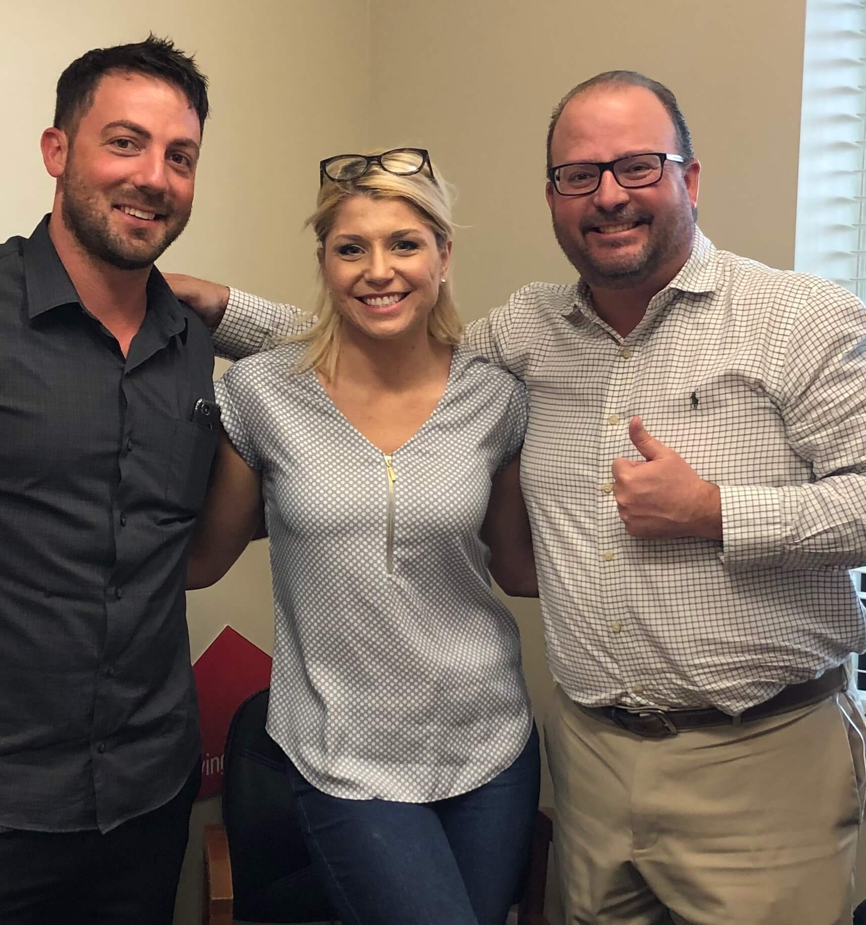 Three people posing for a picture and one of them is giving a thumbs up