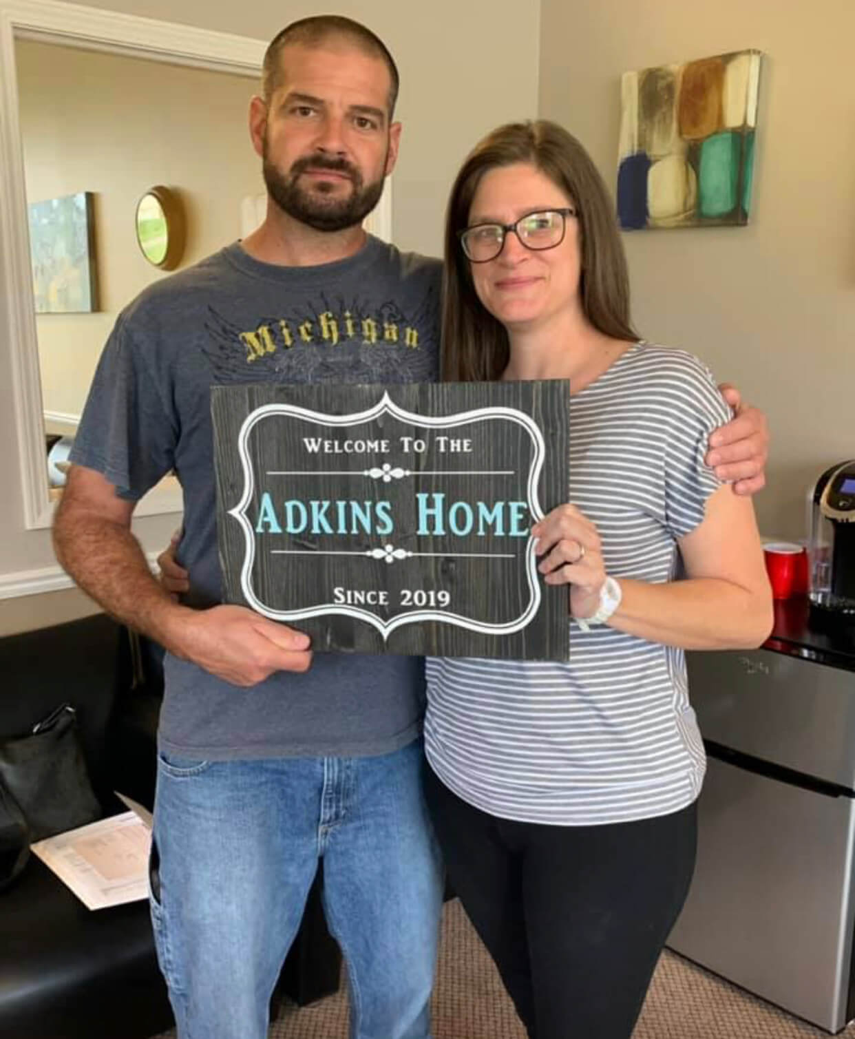 A man and a woman are holding a sign that says `` welcome to the adkins home ''.