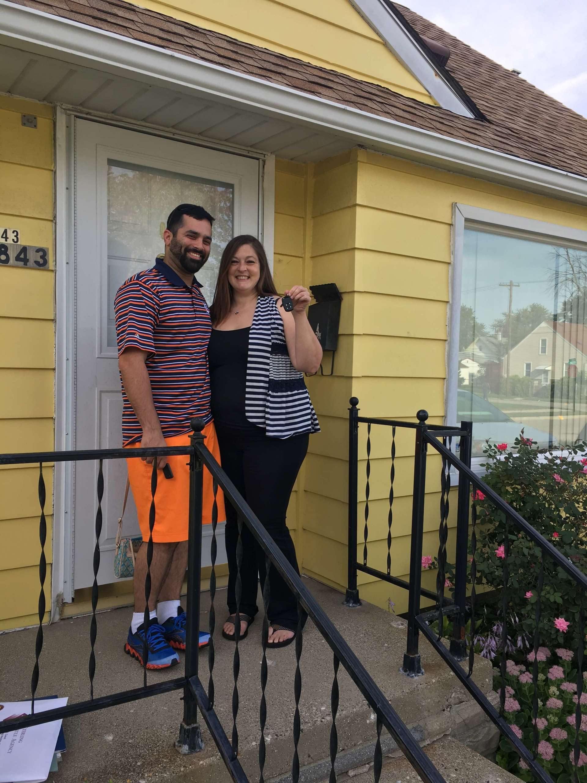A man and woman standing in front of a yellow house