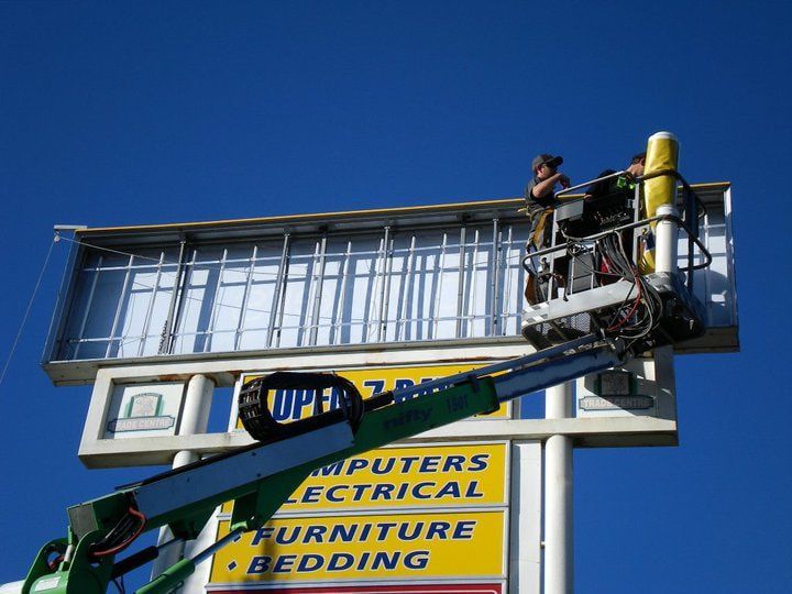 A Man Is Working on A Billboard for Computers Electrical Furniture and Bedding — Signmax Bundaberg In Kensington, QLD
